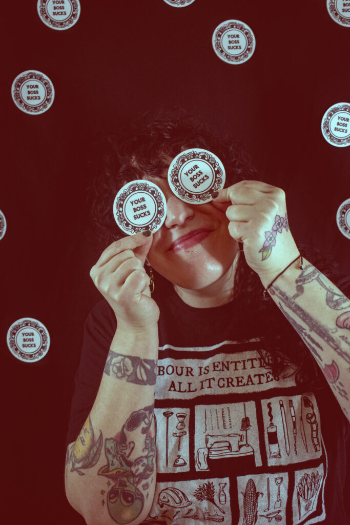 Picture of Tricia holding round stickers in front of her eyes. They read: "You boss sucks."