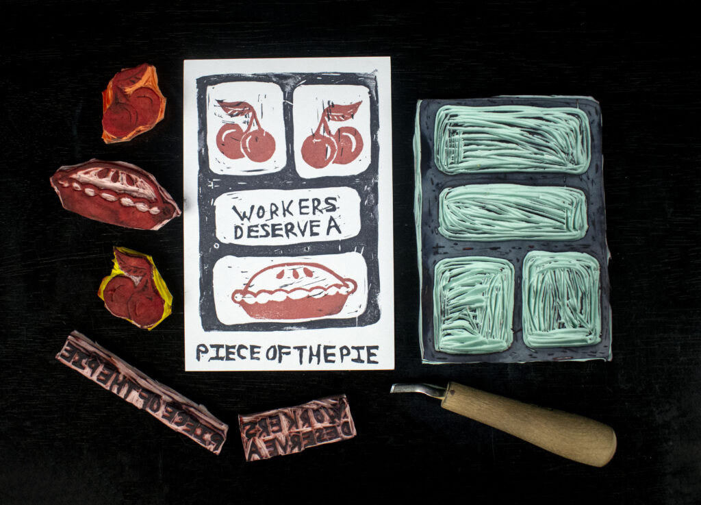 Carved stamps surrounding a print with illustrated cherries and a pie with text that reads: "Workers deserve a piece of the pie."